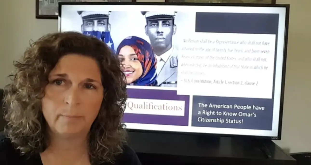 AJ Kern speaking in front of a display about Ilhan Omar’s citizenship.